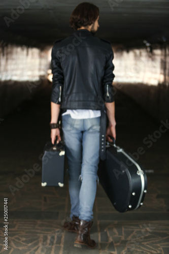 Street musician holding a case with a guitar and amplifier. Rear view. A blurry picture. Vagrant lifestyle. Playing to make money a living. Unemployed musician. Future rock star.