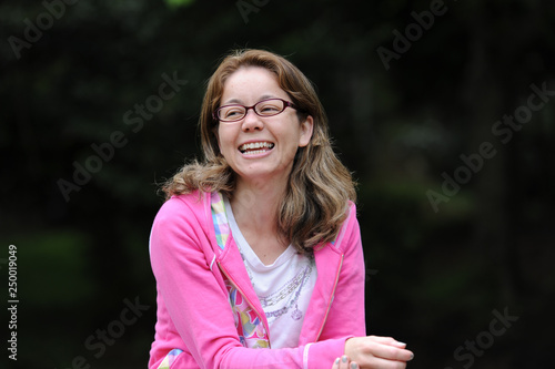 Beautiful mixed race young woman (Brazilian / Japanese) with glasses, smiling and looking to the side. Green blurred background. Space for text.