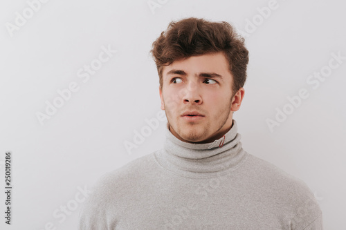 Fotografie young man looks cautiously, isolated background gray, copy space, close-up