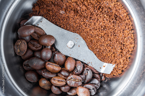 A metal electric coffee grinder. One side of coffee grinder with whole grains of coffee, another with ground. Closeup, selective focus, top view