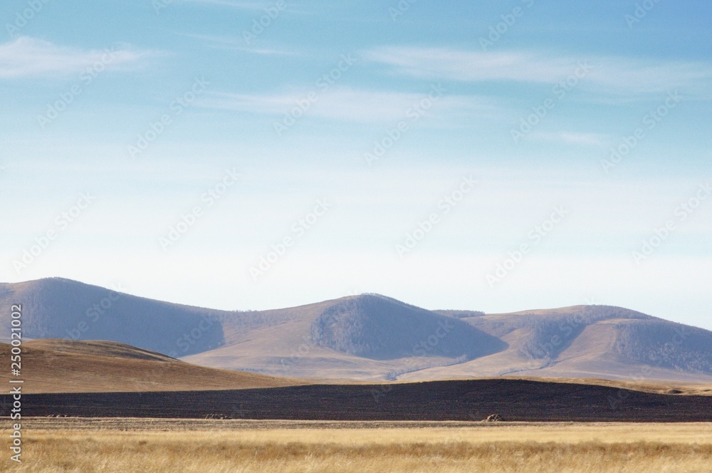 Smooth hills covered with dry grass on horizon with blue sky in Khakassia, Russia