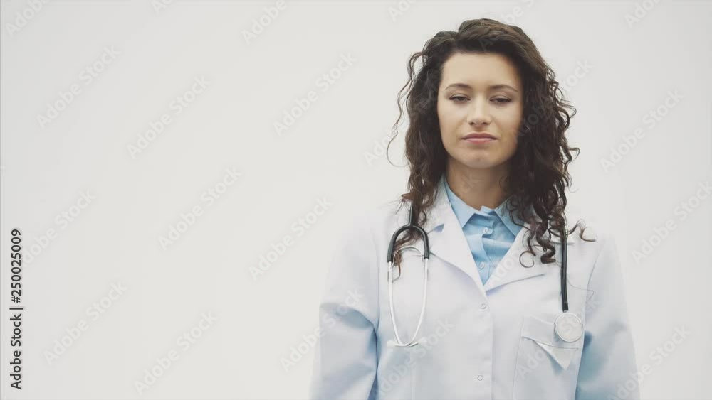 Portrait of happy young smiling girl doctor. Dressed in a white robe. Evenly standing with crossed hands on a gray background. Portrait of happy young smiling girl doctor. Dressed in a white robe. Evenly standing with crossed hands on a gray background.
