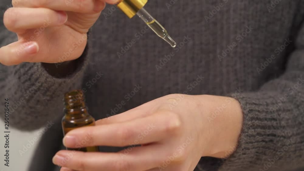 A close-up of woman's hands holding an amber bottle and filling a pipette with oil Hand holding the full pipette above the other hand so that oil droplets are dropping on it. Oil is rubbed into skin A close-up of woman's hands holding an amber bottle and filling a pipette with oil Hand holding the full pipette above the other hand so that oil droplets are dropping on it. Oil is rubbed into skin