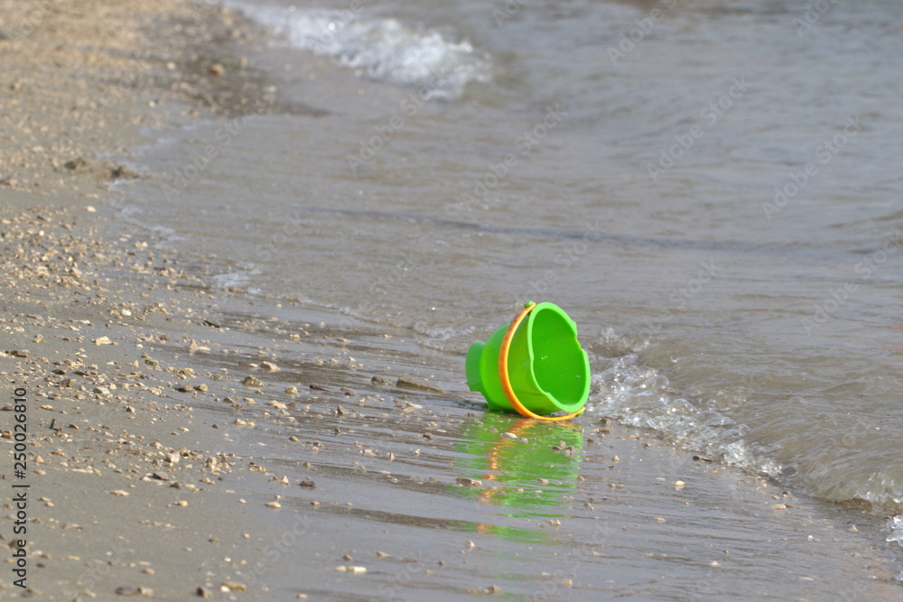 Naklejka premium Green toy bucket lies on the beach