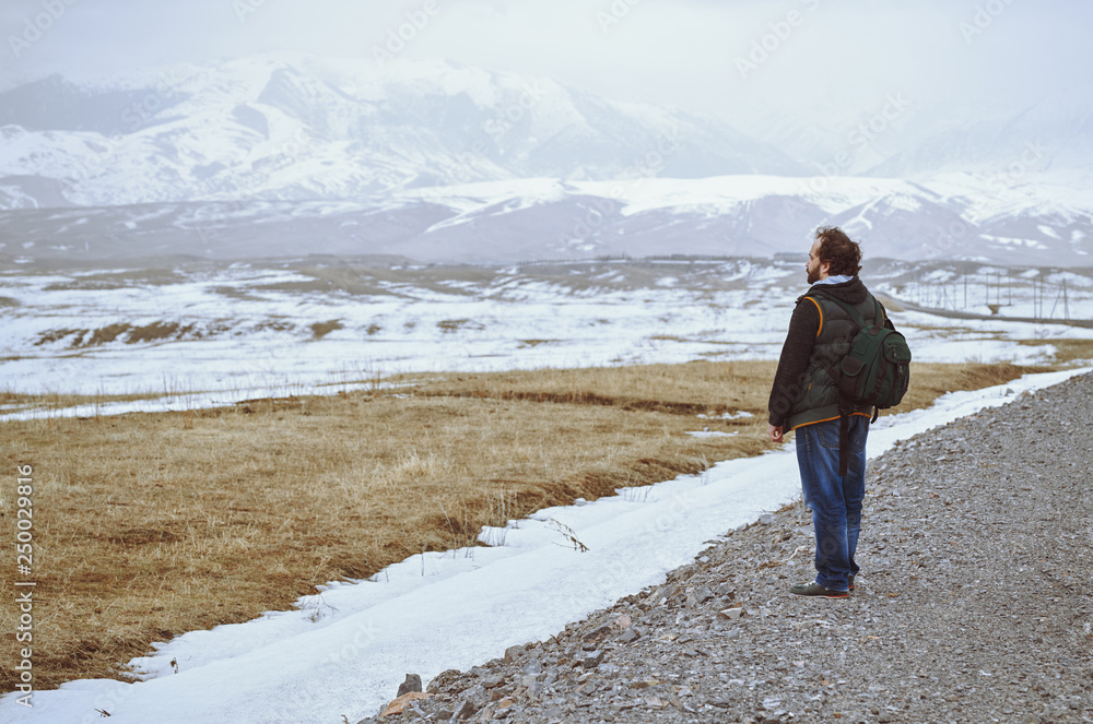 Touris wearing backpack and standing at the rural road while looking at the winter mountains
