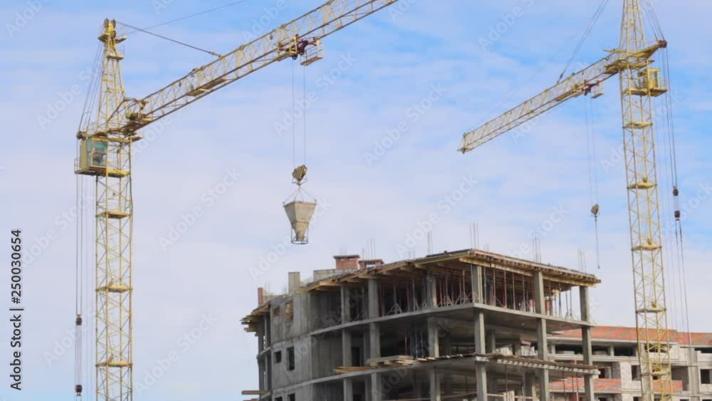 Work tower crane at the construction site. The crane moves the bunker with concrete to the top of the building under construction_ Work tower crane at the construction site. The crane moves the bunker with concrete to the top of the building under construction_