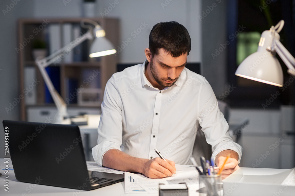 business, deadline and people concept - businessman with laptop computer and papers working at night office business, deadline and people concept - businessman with laptop computer and papers working at night office