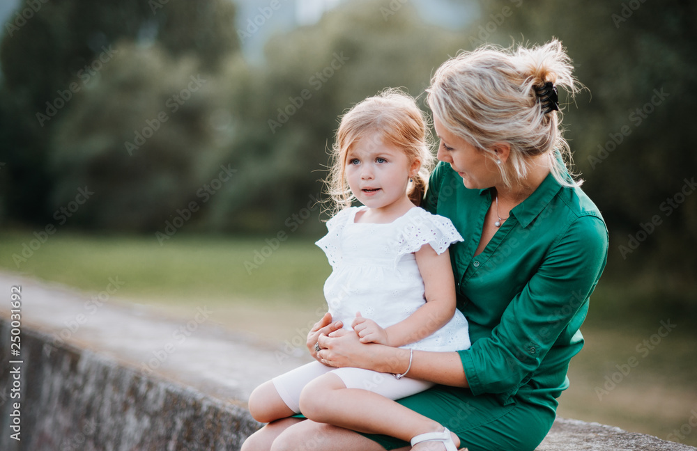 Young mother in nature with small daughter, sitting on a stone wall. Young mother in nature with small daughter, sitting on a stone wall.