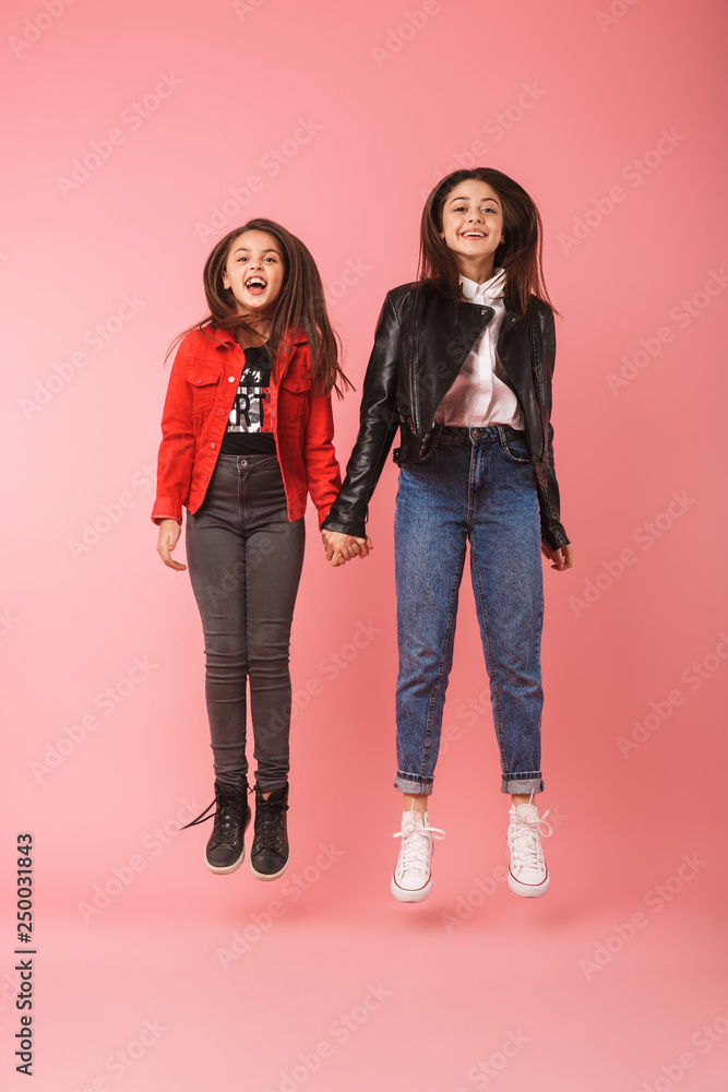 Full length photo of amusing girls in casual jumping together, isolated over red background Full length photo of amusing girls in casual jumping together, isolated over red background