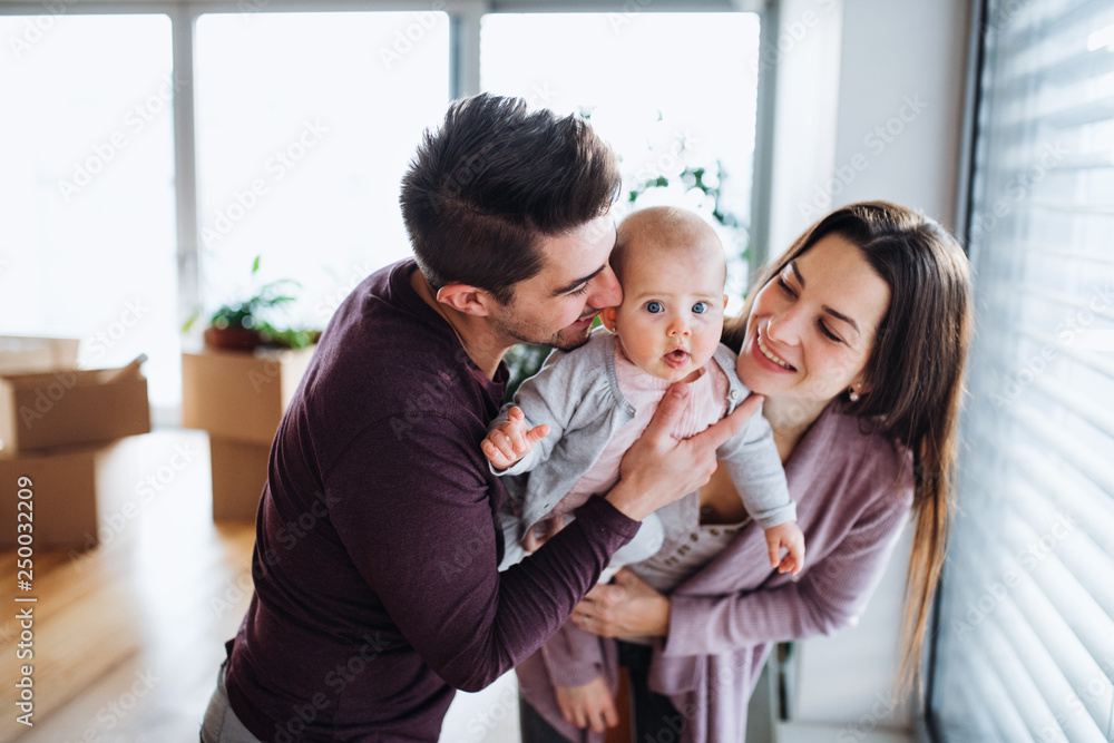 A portrait of young couple with a baby and cardboard boxes moving in a new home. A portrait of young couple with a baby and cardboard boxes moving in a new home.