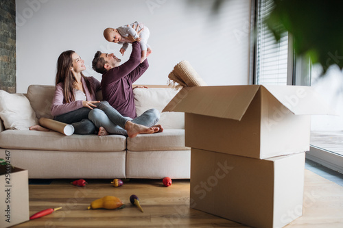 A portrait of young couple with a baby and cardboard boxes moving in a new home. photo