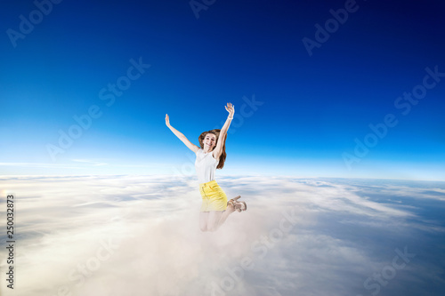 Young woman jumps in the blue cloudy sky.