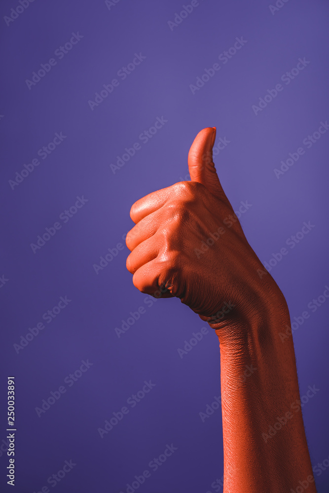 partial view of woman showing thumb up on coral colored hand on violet background, color of 2019 concept