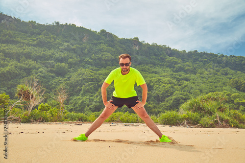 Sportsman stretching on a tropical sandy beach. © astrosystem