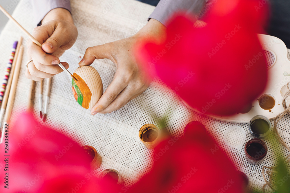Happy Easter concept. Hands holding and painting easter egg on rustic table with paint,brushes, tulips bouquet, space for text. Decorating easter egg, holiday preparations. Happy Easter concept. Hands holding and painting easter egg on rustic table with paint,brushes, tulips bouquet, space for text. Decorating easter egg, holiday preparations.