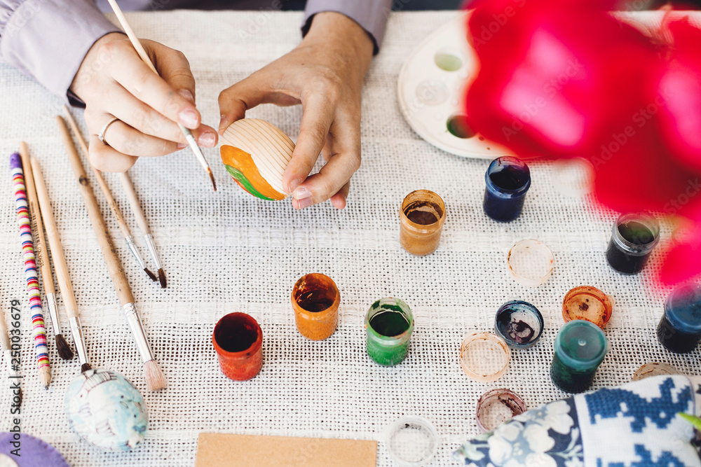 Happy Easter concept, flat lay. Hands holding and painting easter egg on rustic table with paint,brushes, tulips bouquet, space for text. Child decorating easter egg, holiday preparations Happy Easter concept, flat lay. Hands holding and painting easter egg on rustic table with paint,brushes, tulips bouquet, space for text. Child decorating easter egg, holiday preparations