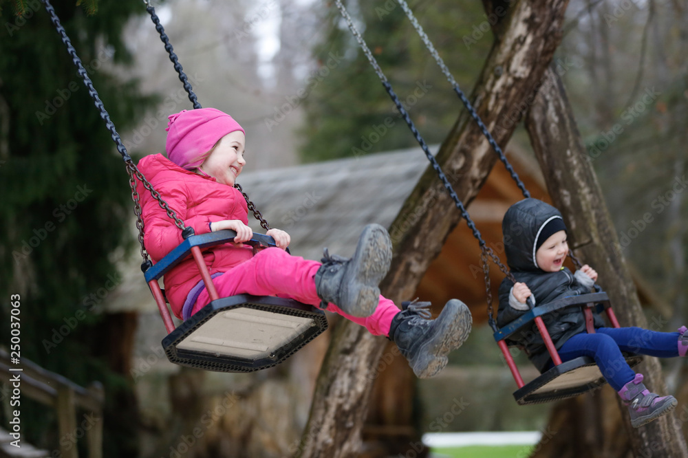 Obraz premium Little brother and sister laughing while having fun on a swing. Concept of freedom, carefree childhood, spending time outdoor.