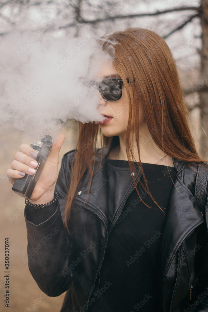 The girl in sunglasses lets out steam from the mouth. Redhead vape girl.