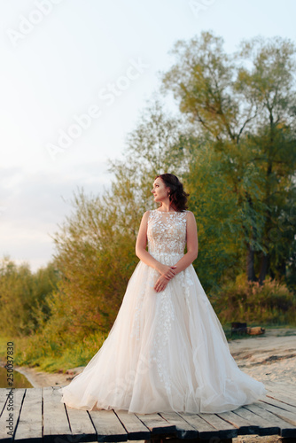 young beautiful bride in white dress on wooden pier near water at sunset © ShevarevAlex