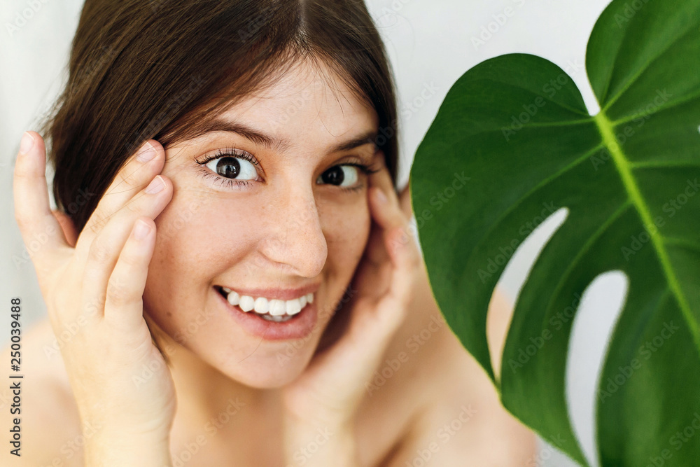 Eye Skin Care and Treatment. Portrait of beautiful young happy woman holding hands at eyes skin at green palm leaf. Girl enjoying skin effect after lifting anti-wrinkle collagen patches under eyes Eye Skin Care and Treatment. Portrait of beautiful young happy woman holding hands at eyes skin at green palm leaf. Girl enjoying skin effect after lifting anti-wrinkle collagen patches under eyes