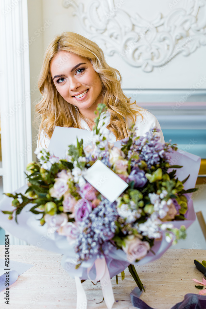 selective focus of beautiful smiling woman with flower bouquet with roses, lilac and blank card on foreground selective focus of beautiful smiling woman with flower bouquet with roses, lilac and blank card on foreground