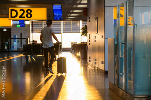 Man walking towards airport gate with roller suitcase