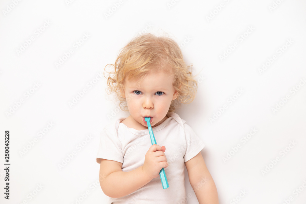 Caucasian little cute curly baby girl in white clothes body brushing her teeth with a colored blue brush on a white background. Caucasian little cute curly baby girl in white clothes body brushing her teeth with a colored blue brush on a white background.