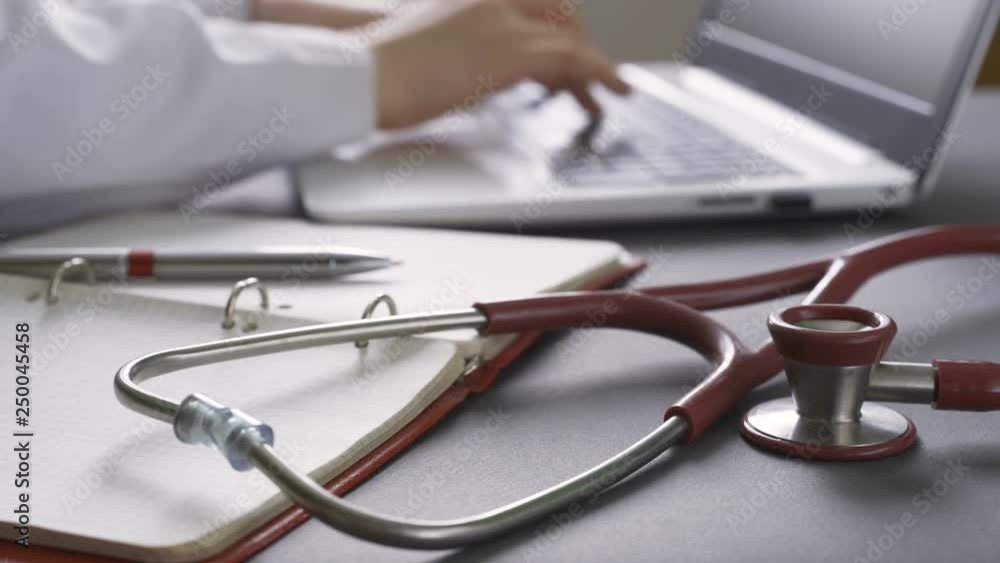 Close up of doctor working at the workplace on laptop. Stethoscope on foreground. Close up of doctor working at the workplace on laptop. Stethoscope on foreground.