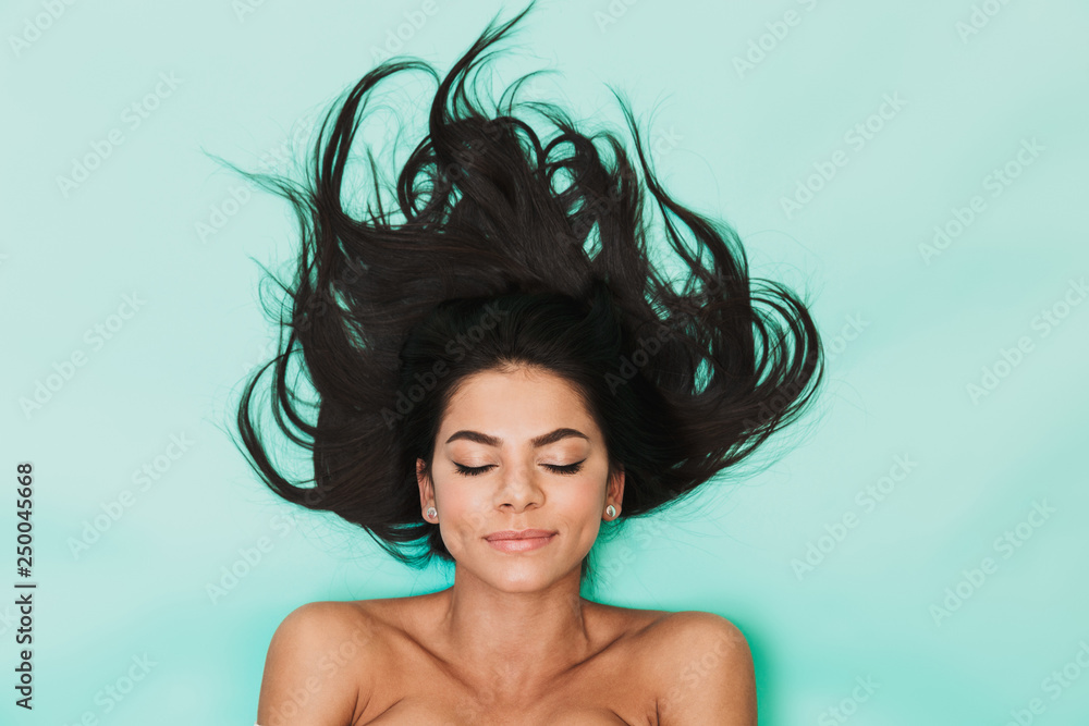 Beautiful young woman lies isolated on blue light background. Healthy hair concept. - obrazy, fototapety, plakaty 