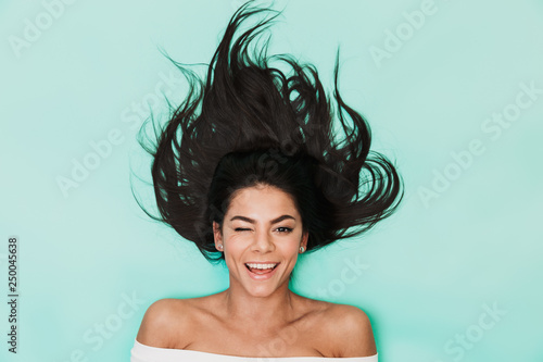 Beautiful young woman lies isolated on blue light background. Healthy hair concept.