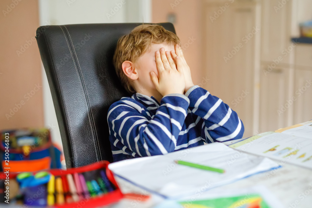 Portrait of frustrated crying sad school kid boy at home making homework. Little child writing with colorful pencils, indoors. Elementary school and education, heavy burden at school Portrait of frustrated crying sad school kid boy at home making homework. Little child writing with colorful pencils, indoors. Elementary school and education, heavy burden at school