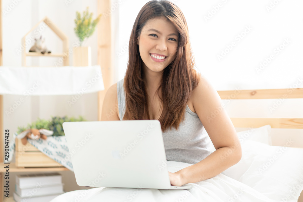Happy young Asian woman working with a laptop in the bedroom Happy young Asian woman working with a laptop in the bedroom