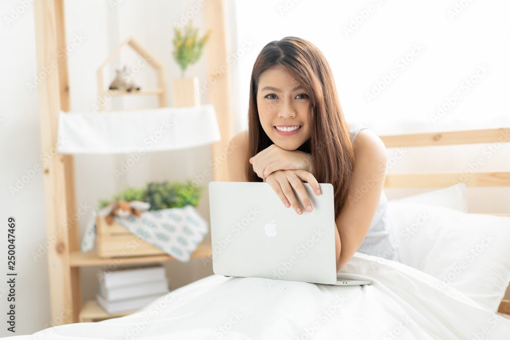 Happy young Asian woman working with a laptop in the bedroom Happy young Asian woman working with a laptop in the bedroom