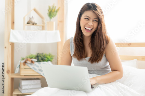 Happy young Asian woman working with a laptop in the bedroom