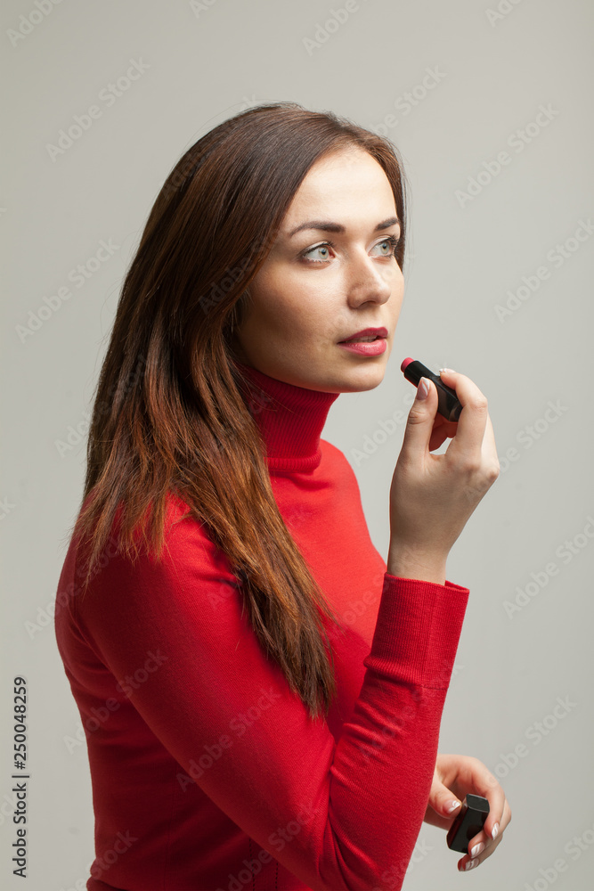 Beautiful young woman in red sweater applying lipstick. Pretty woman going to job. Preparing for a date or meeting. Skincare. Makeup. Beautiful young woman in red sweater applying lipstick. Pretty woman going to job. Preparing for a date or meeting. Skincare. Makeup.