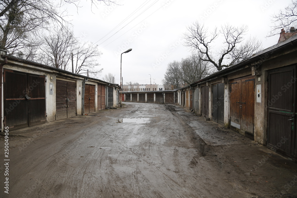 Old, neglected, ruined garages. Muddy, holey, uneven road with puddles. Winter, autumn landscape in the city. Wrocław, Wroclaw, Breslau.Lower Silesia, Dolny Śląsk. Polska, Poland, Polen. Old, neglected, ruined garages. Muddy, holey, uneven road with puddles. Winter, autumn landscape in the city. Wrocław, Wroclaw, Breslau.Lower Silesia, Dolny Śląsk. Polska, Poland, Polen.