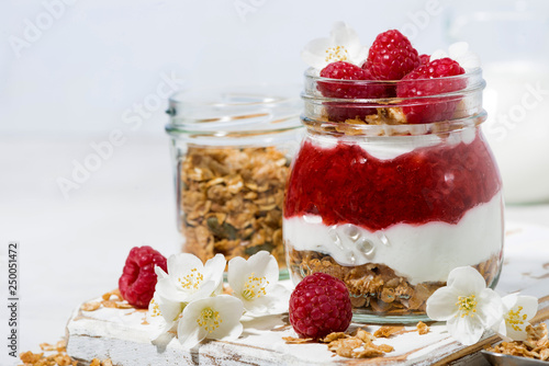 desserts with granola, and raspberries puree in jar on white wooden board