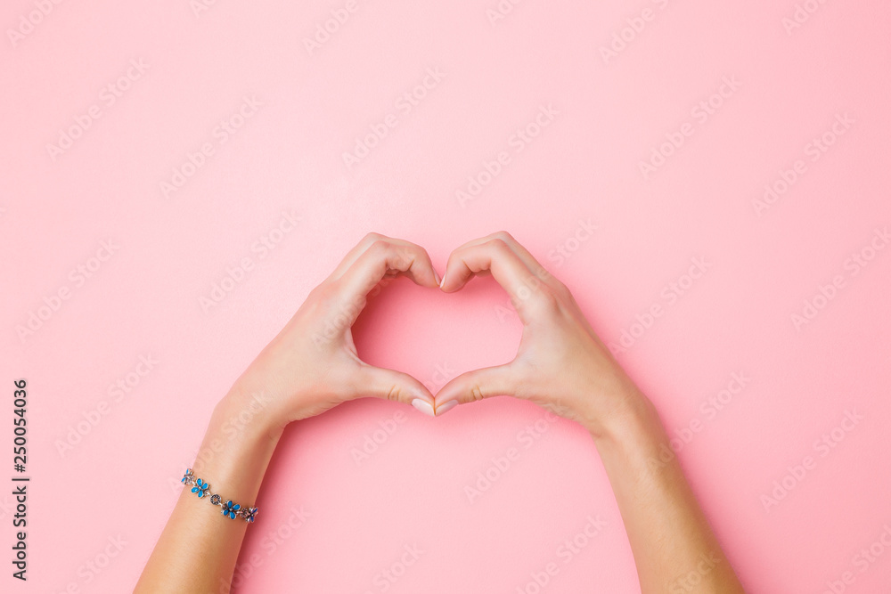 Heart shape created from young woman's hands on pastel pink background. Love and happiness concept. Empty place for emotional, sentimental text, quote or sayings. Closeup. Top view. - obrazy, fototapety, plakaty 