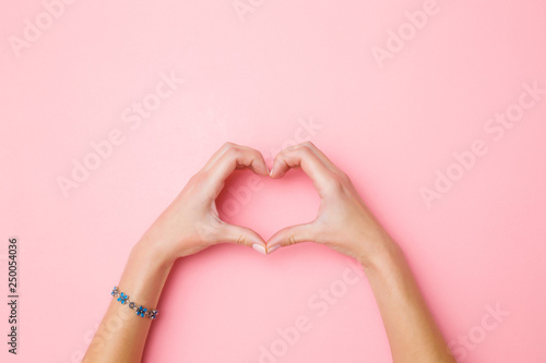 Heart shape created from young woman's hands on pastel pink background. Love and happiness concept. Empty place for emotional, sentimental text, quote or sayings. Closeup. Top view.