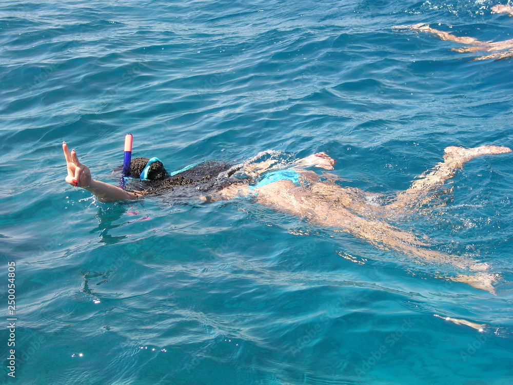 Beautiful woman swims in the Red Sea and engaged in snorkelling with a snorkel and mask. And she shows the Victory sign with fingers Beautiful woman swims in the Red Sea and engaged in snorkelling with a snorkel and mask. And she shows the Victory sign with fingers