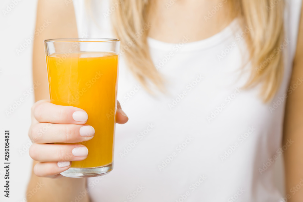 Young blonde woman in white shirt. Hand holding glass of orange juice. Tasty, healthy drink. Front view. Closeup. Young blonde woman in white shirt. Hand holding glass of orange juice. Tasty, healthy drink. Front view. Closeup.