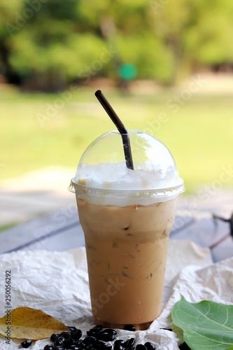 Iced coffee in plastic glasses on white paper with coffee bean and leaves on a black wooden table.