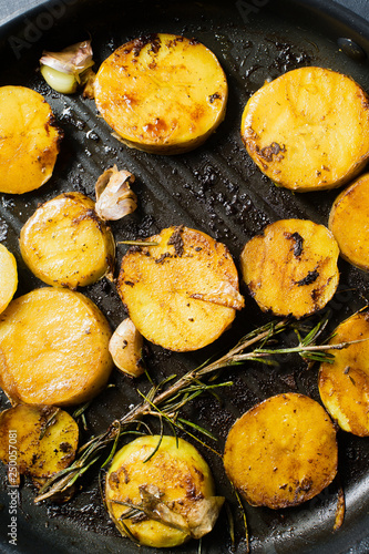American traditional fried potatoes with garlic and rosemary in a frying pan. Top view, black background, close up.