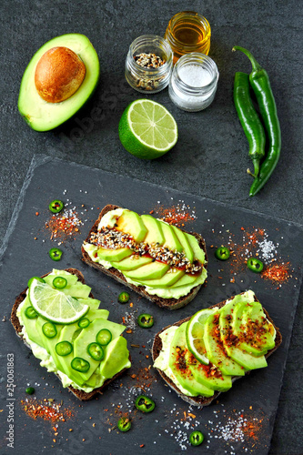 Healthy avocado toasts with spices, lime and chili, presented on a gray stone board.