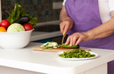 An old woman cutting fresh vegetables in the kitchen. Healthy eating. Preparation of salad. 