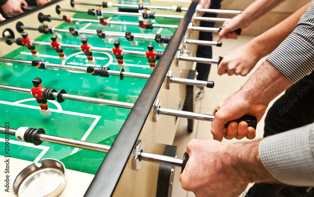 Guys are  playing table soccer indoor