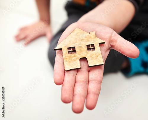 A little child holds wooden flat house in his hands on the white background © SkyLine