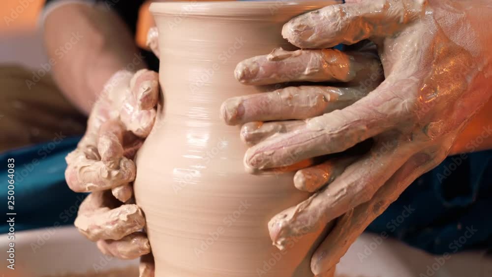 Hands of potter and his female student. Man and woman working together, creating clay product on potter wheel. Traditional pottery making, teacher shows basics of pottery in art studio Hands of potter and his female student. Man and woman working together, creating clay product on potter wheel. Traditional pottery making, teacher shows basics of pottery in art studio