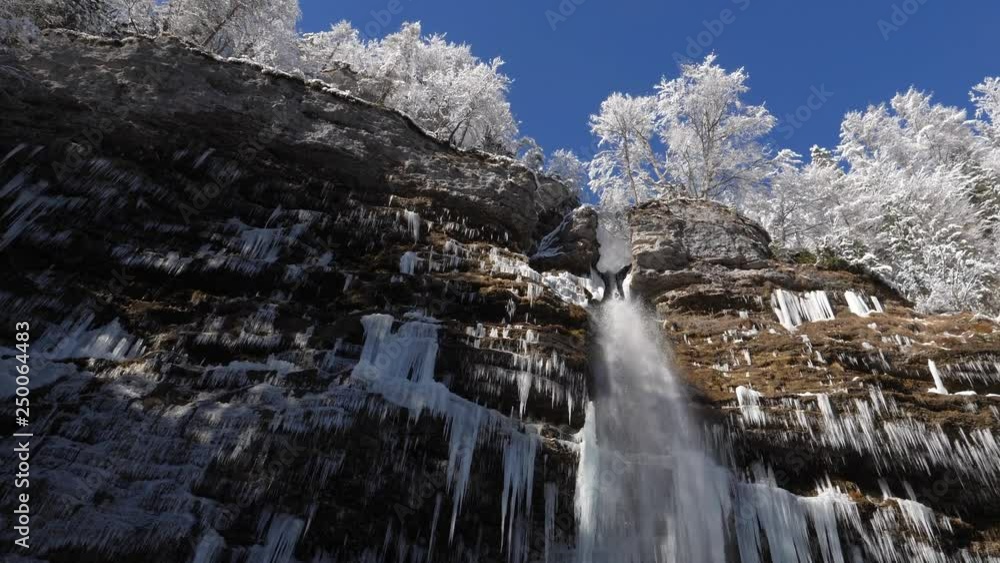 NATURE BACKGROUND, SLOW MOTION 4K Camera pan left to right in winter wonderland with magical waterfall falling over a cliff face in the Julian Alps, Slovenia. Waterfall falling past numerous white ici NATURE BACKGROUND, SLOW MOTION 4K Camera pan left to right in winter wonderland with magical waterfall falling over a cliff face in the Julian Alps, Slovenia. Waterfall falling past numerous white ici