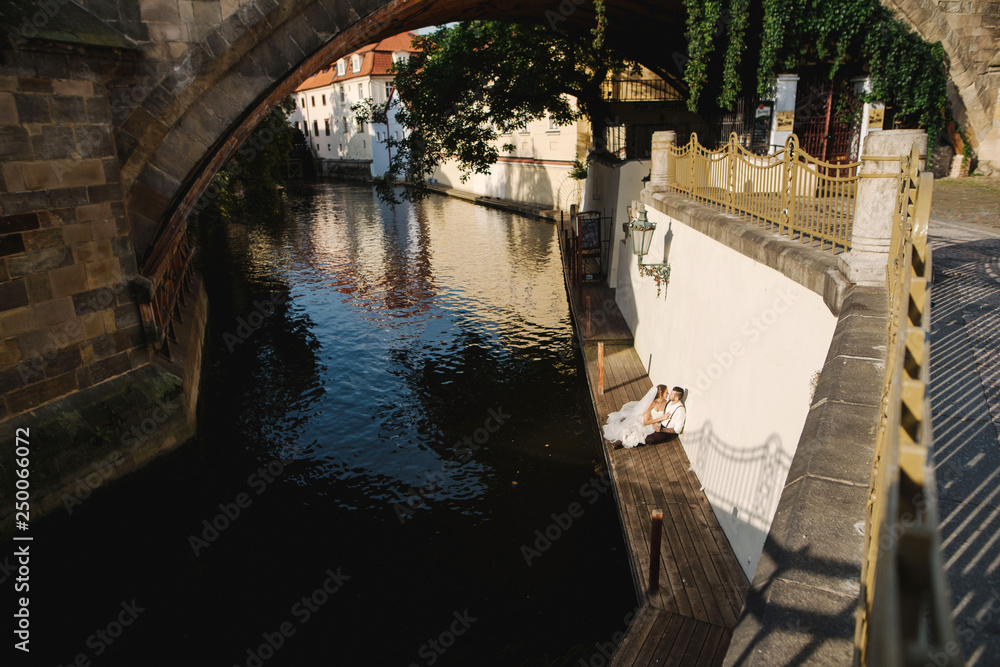 Wedding couple sitting on the wooden dock near the river channel in the Prague, Czech Republic